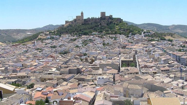 Vista panorámica de Alcalá la Real con la fortaleza de la Mota en lo alto de una colina y el caserío blanco extendiéndose al pie bajo un cielo despejado.