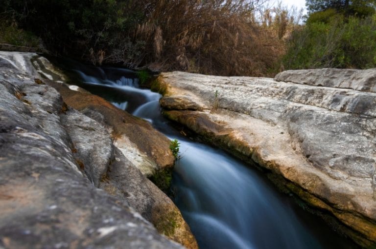 Vista del estrecho de Bolvonegro con un río de agua clara fluyendo entre rocas y vegetación en un entorno natural