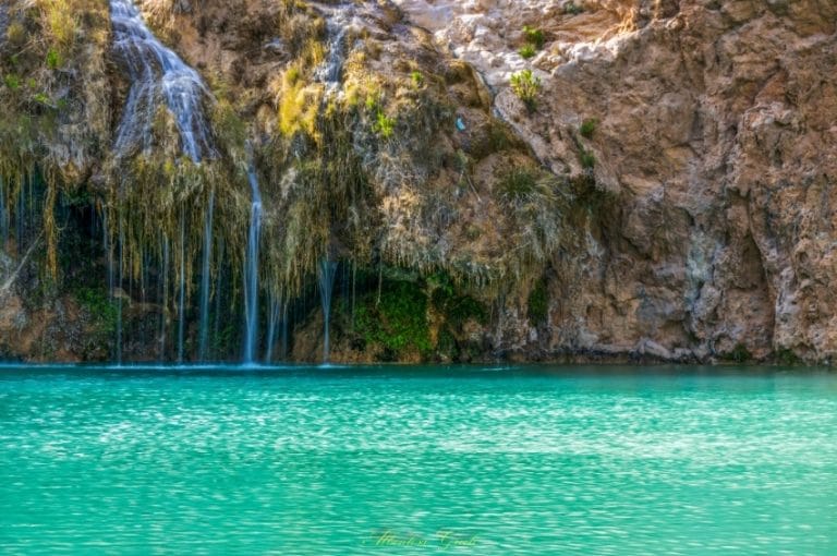 Cascada pequeña en la fuente Caputa con piscina natural de agua turquesa rodeada de rocas y vegetación