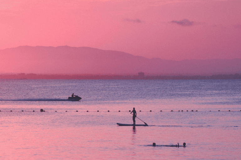 Silueta de una persona practicando paddle surf en el Mar Menor durante un atardecer rosado en La Manga.