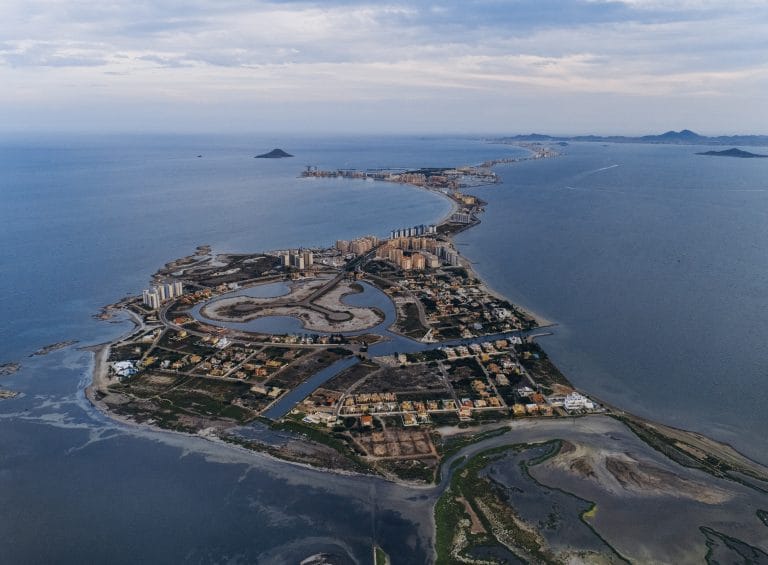 Vista aérea de La Manga del Mar Menor, con su estrecha franja de tierra entre el Mediterráneo y la laguna, mostrando urbanizaciones, canales y marismas.