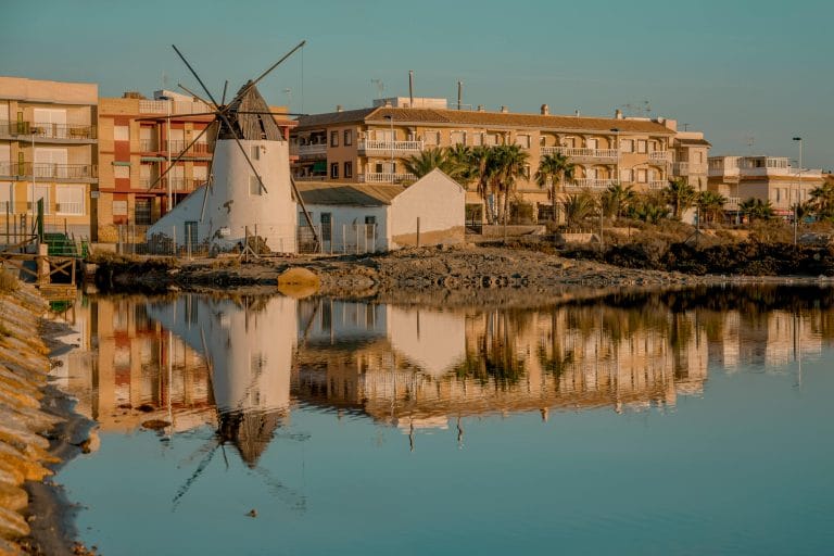 Molino del Agua de San Pedro del Pinatar junto a edificios, reflejado en la laguna salina al atardecer.