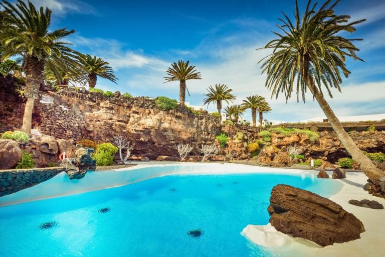 Piscina en los Jameos del Agua en Lanzarote, rodeada de palmeras y formaciones volcánicas, diseño de César Manrique