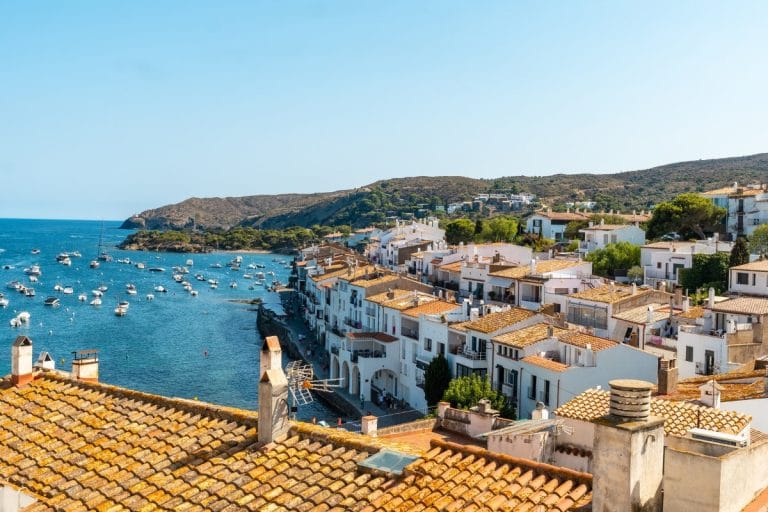 Vista panorámica de Cadaqués con sus casas blancas, tejados rojizos y el mar Mediterráneo salpicado de barcas en la Costa Brava.