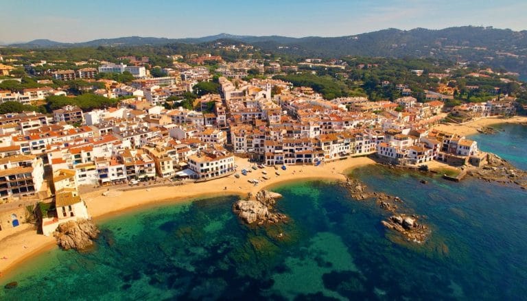 Vista aérea del centro histórico de Calella de Palafrugell con casas blancas, barcas en la arena y aguas cristalinas en la Costa Brava.