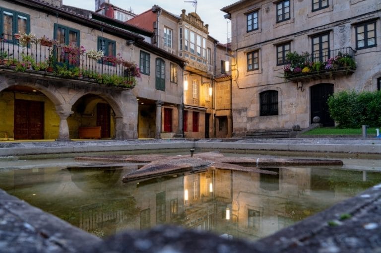 Vista nocturna del casco antiguo de Pontevedra con fuente en primer plano y casas con soportales y balcones floridos