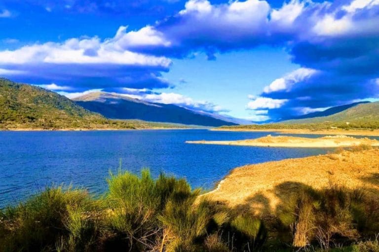 Vista del embalse de Plasencia rodeado de montañas y vegetación bajo un cielo parcialmente nublado
