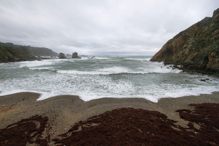 Vista de la Playa del Silencio en la costa occidental de Asturias, con mar agitado y formaciones rocosas bajo cielo nublado
