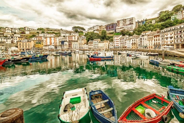 Puerto de Luarca con barcos de pesca y casas coloridas reflejadas en el agua, en la costa occidental de Asturias