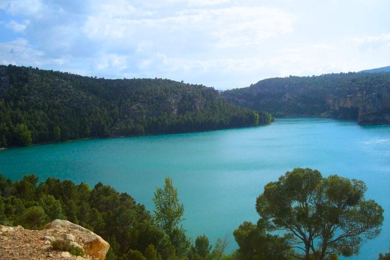 Vista panorámica del embalse de Santolea, con sus aguas turquesas rodeadas de colinas boscosas y vegetación mediterránea bajo un cielo parcialmente nublado.